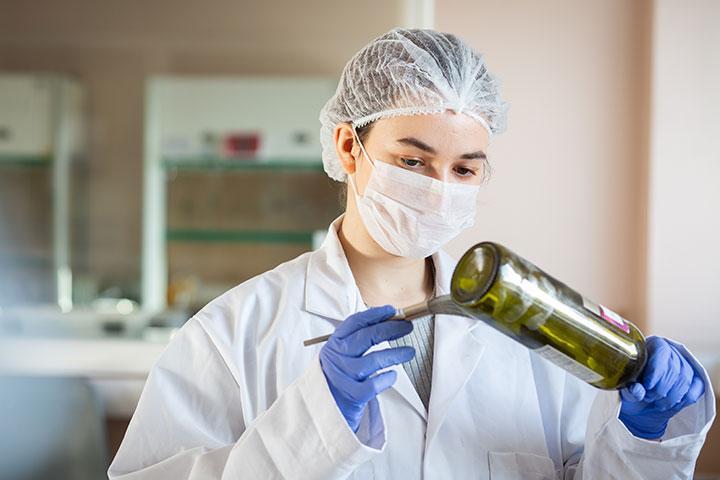 A student dusting a wine bottle for fingerprints.