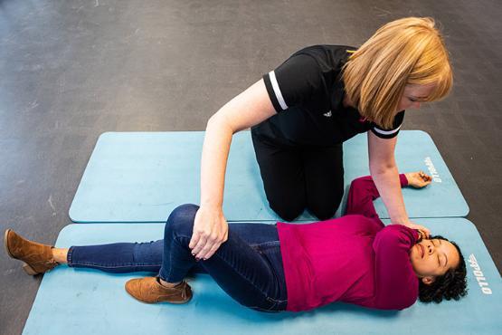 A First Aid staff member puts a student in the recovery position on a mat
