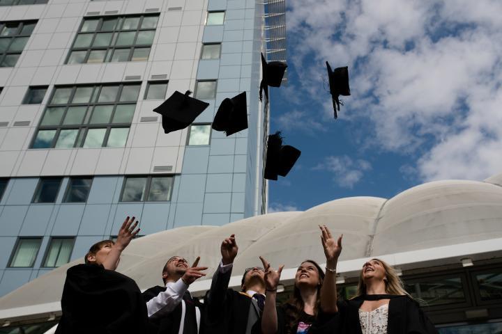Graduates throwing their graduation caps into the air outside the University of Bradford Richmond building