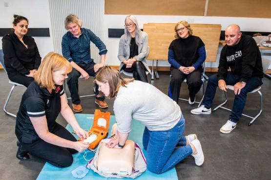 A group of people observing a first aid CPR demonstration